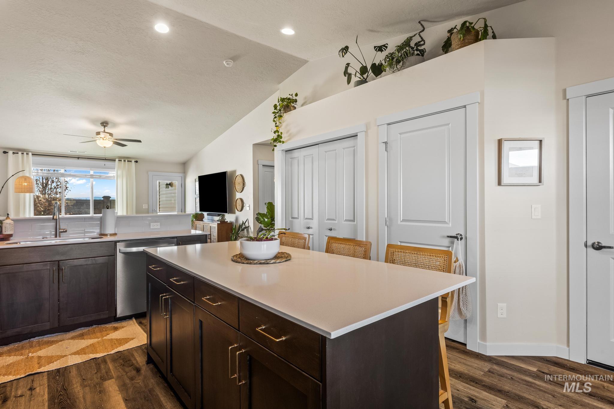Kitchen featuring a breakfast bar area, dark brown cabinetry, dishwasher, dark wood-style floors, and vaulted ceiling