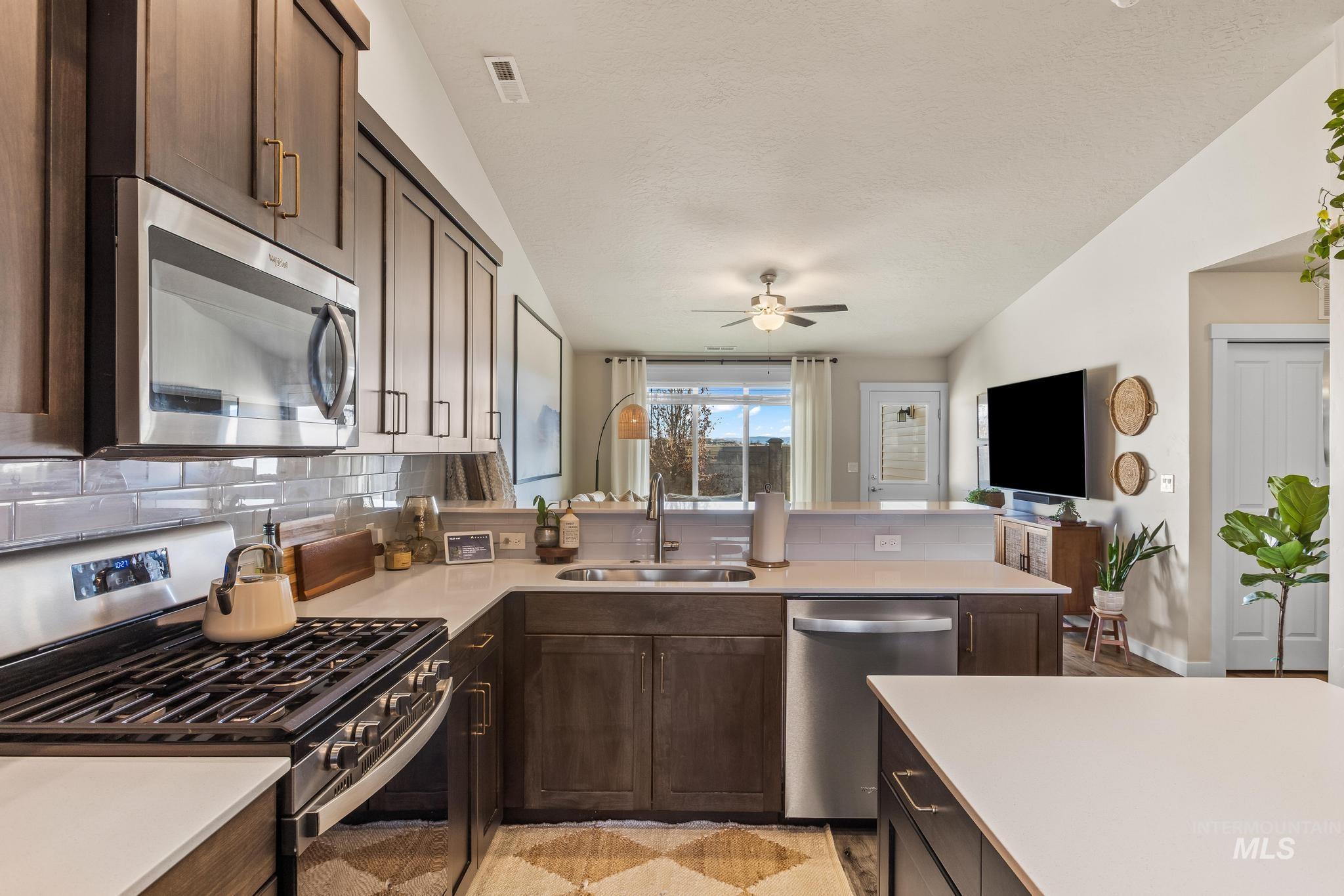 Kitchen featuring appliances with stainless steel finishes, dark brown cabinetry, tasteful backsplash, a peninsula, and open floor plan