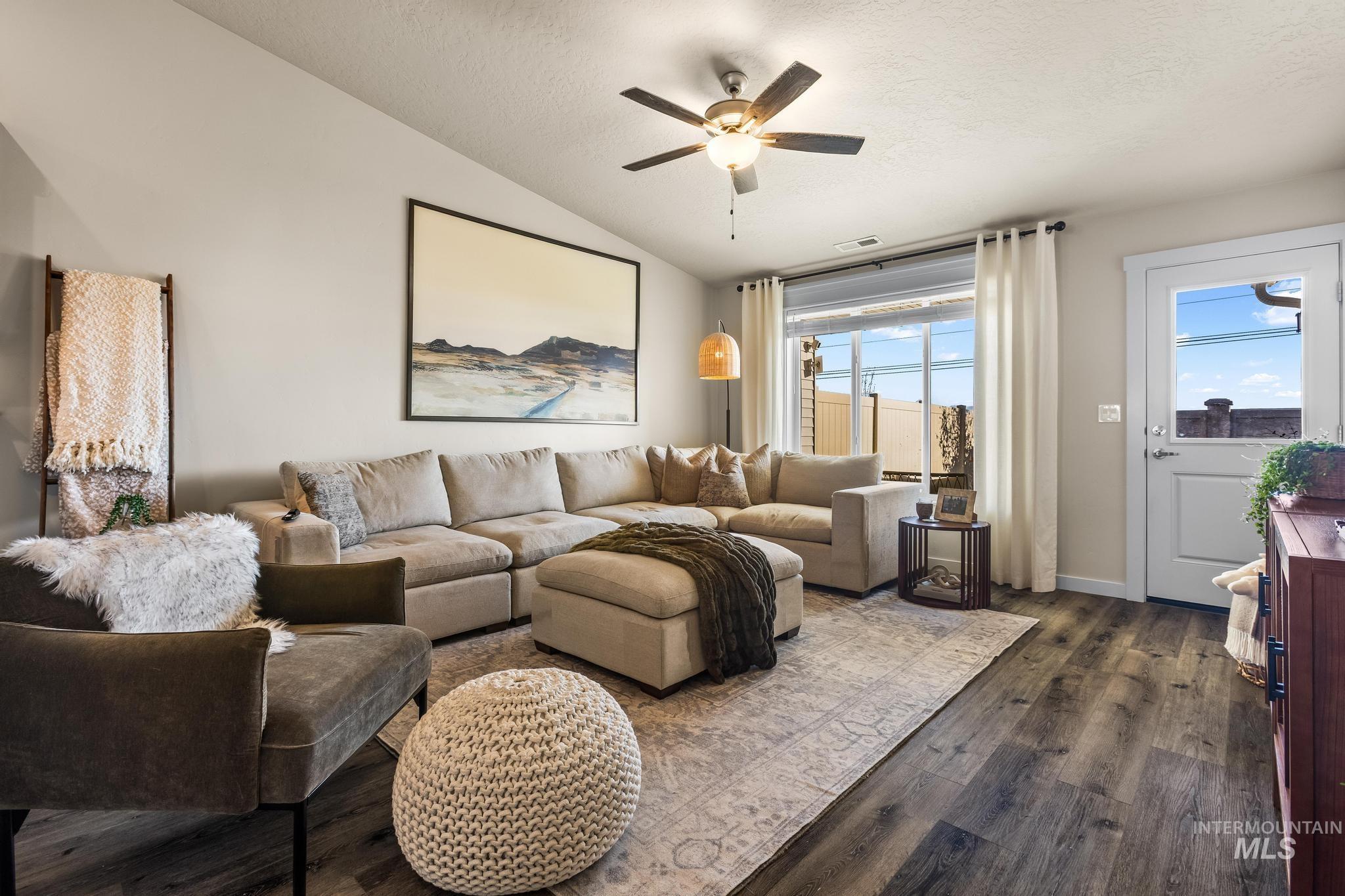 Living area featuring vaulted ceiling, dark wood-type flooring, a textured ceiling, and a ceiling fan