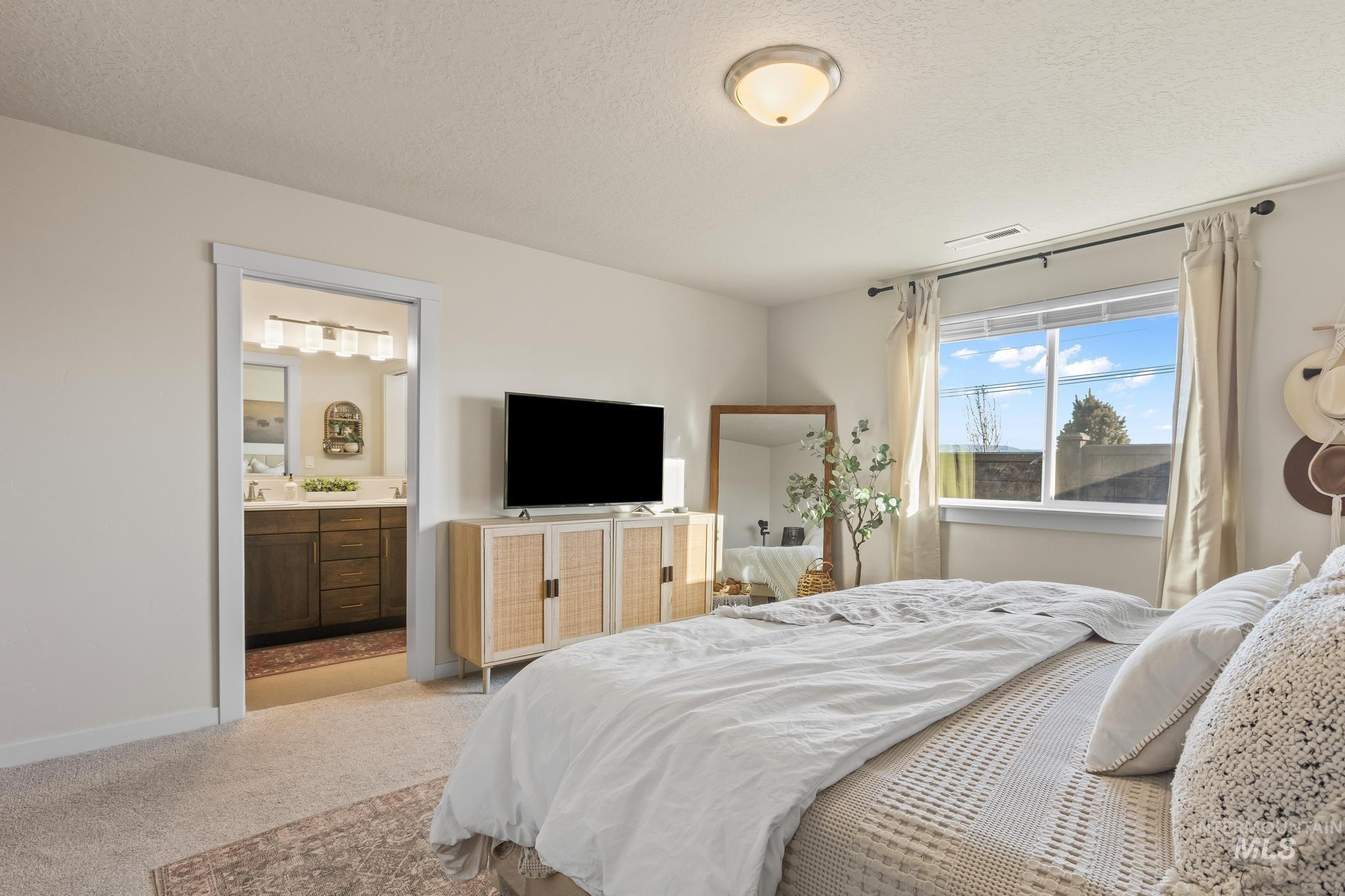 Bedroom with a textured ceiling, light colored carpet, and ensuite bathroom