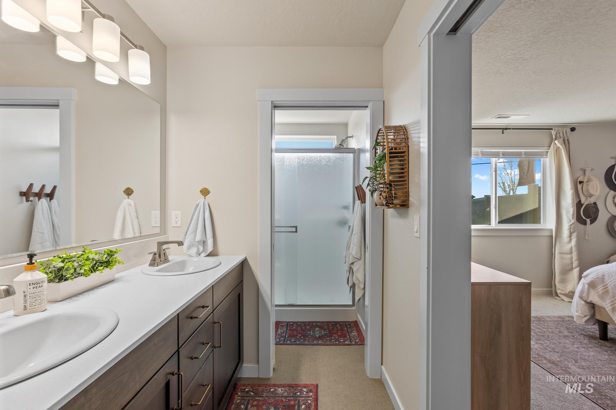 Ensuite bathroom featuring double vanity, a stall shower, a textured ceiling, and light flooring
