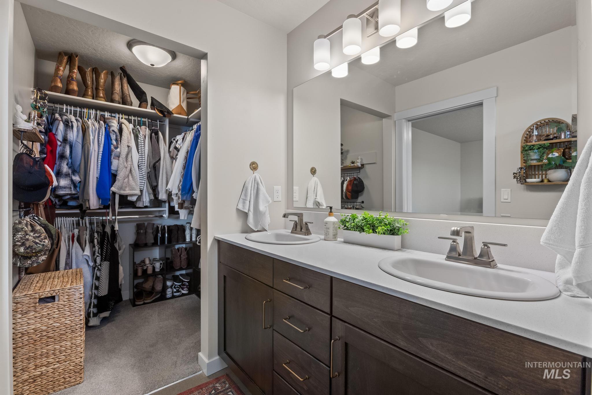 Full bath with double vanity, a spacious closet, and dark colored carpet