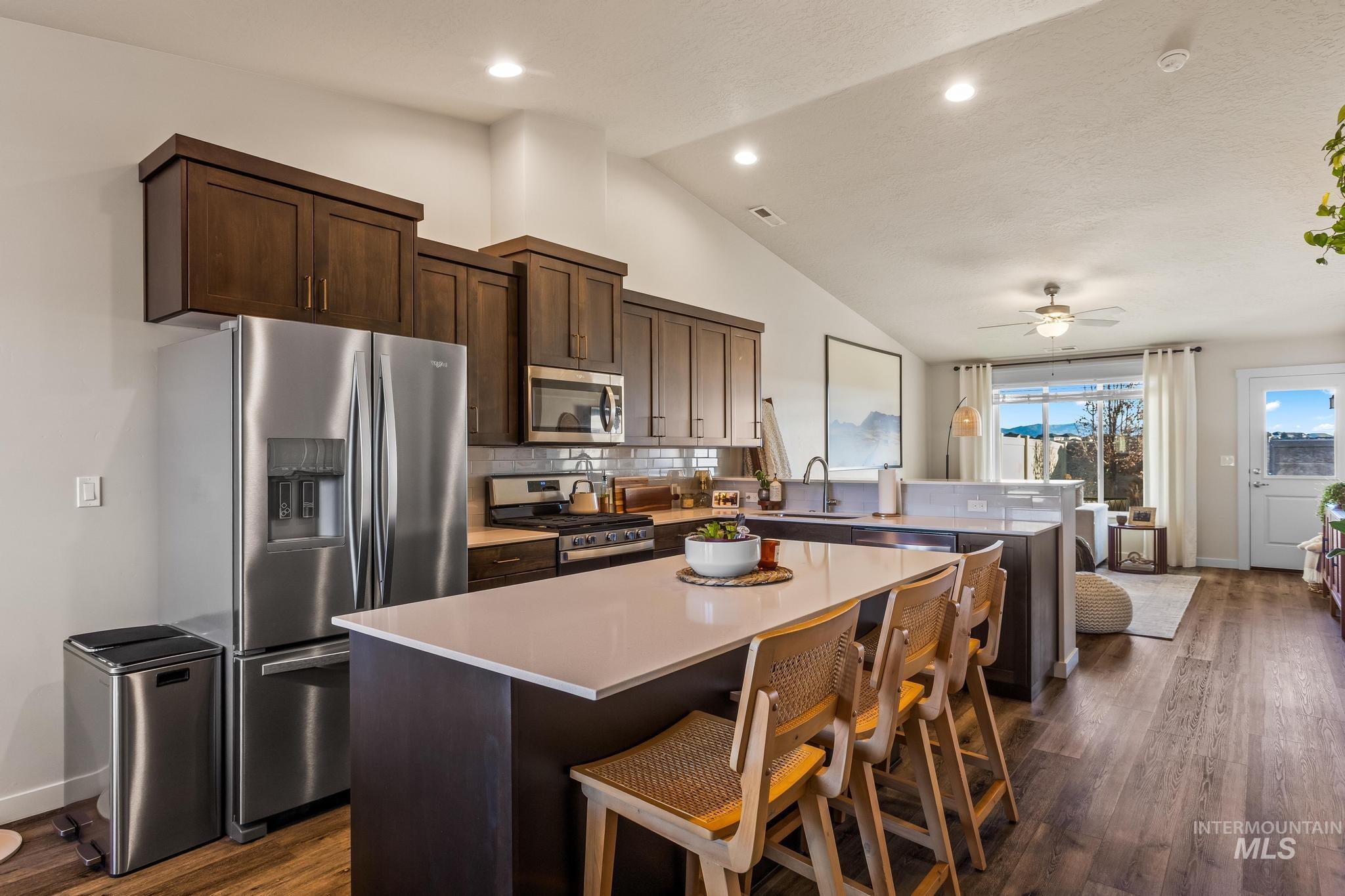 Kitchen with dark brown cabinetry, stainless steel appliances, a kitchen island, a breakfast bar area, and dark wood-style flooring