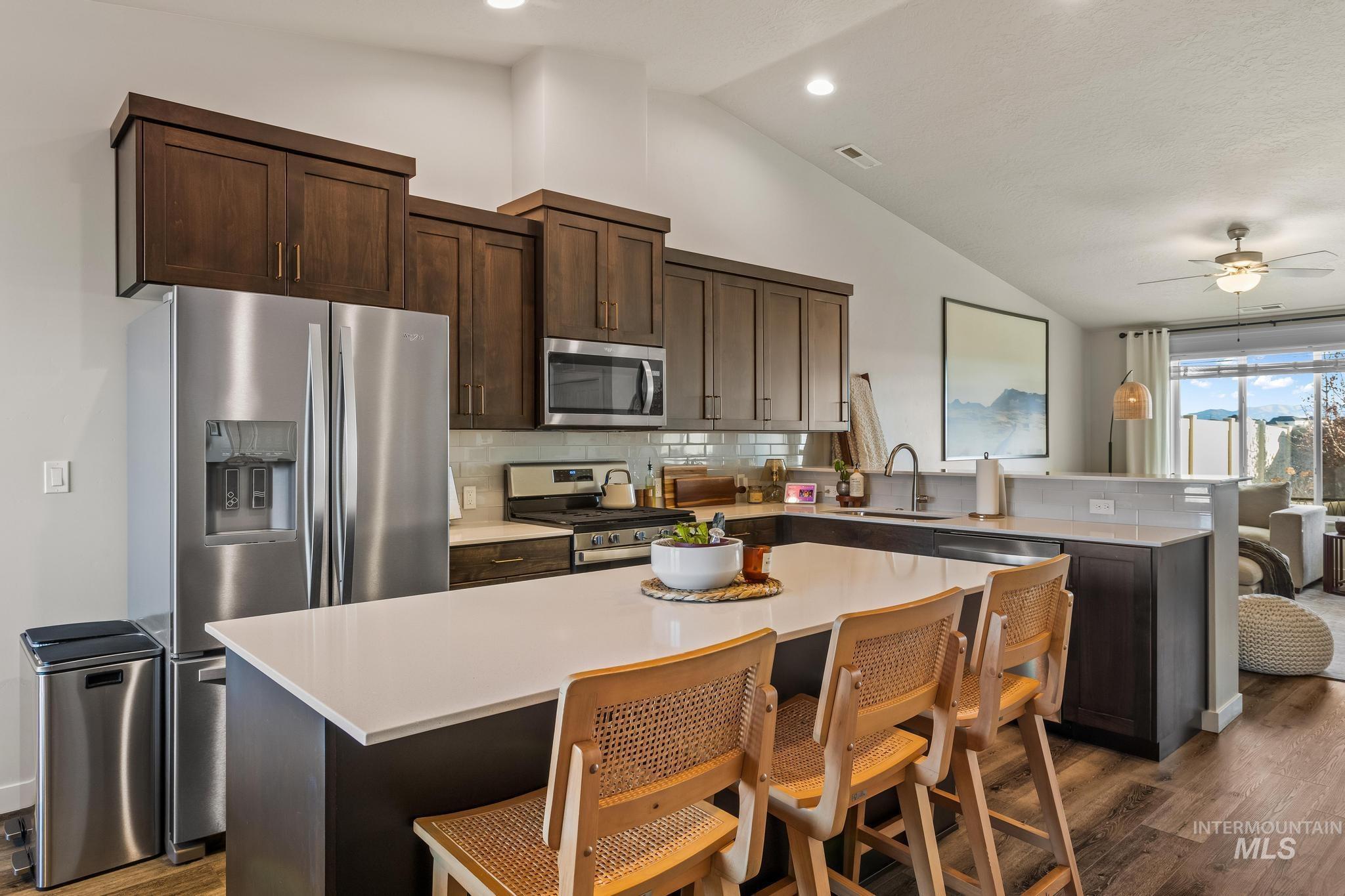 Kitchen featuring dark brown cabinetry, stainless steel appliances, a center island, a kitchen bar, and backsplash