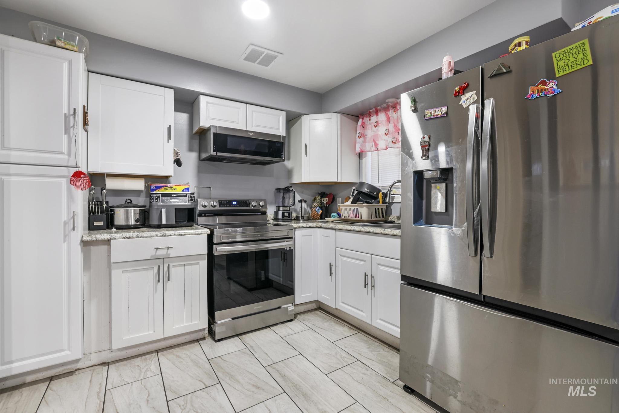 Kitchen with stainless steel appliances, white cabinets, and light stone countertops