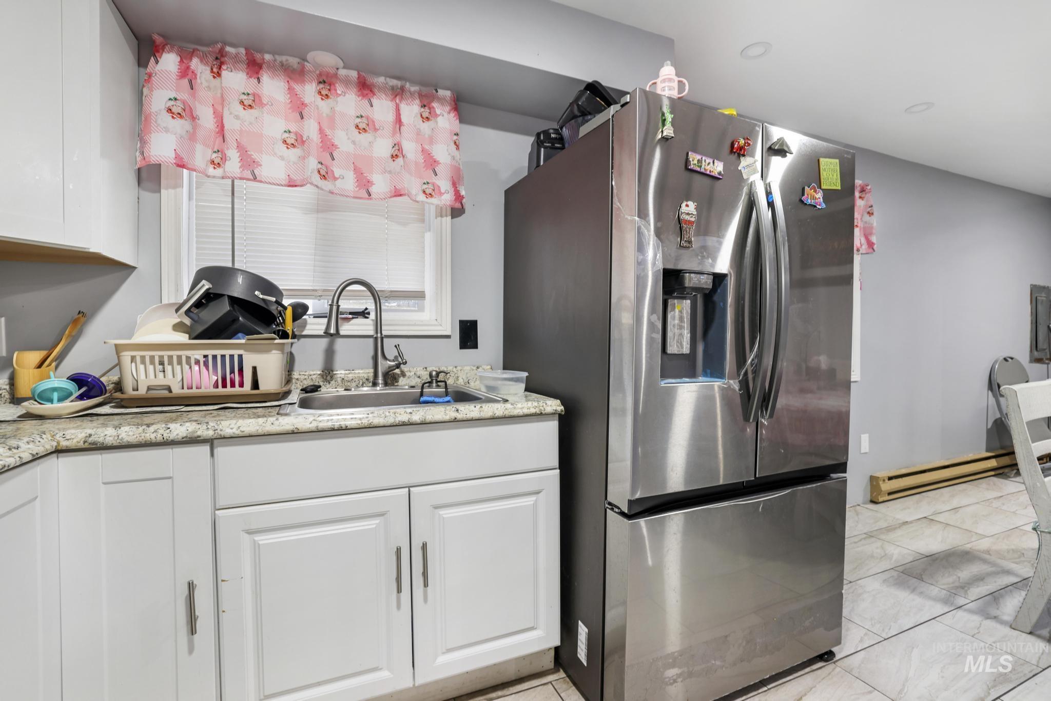 Kitchen featuring stainless steel refrigerator with ice dispenser, white cabinetry, and a baseboard heating unit