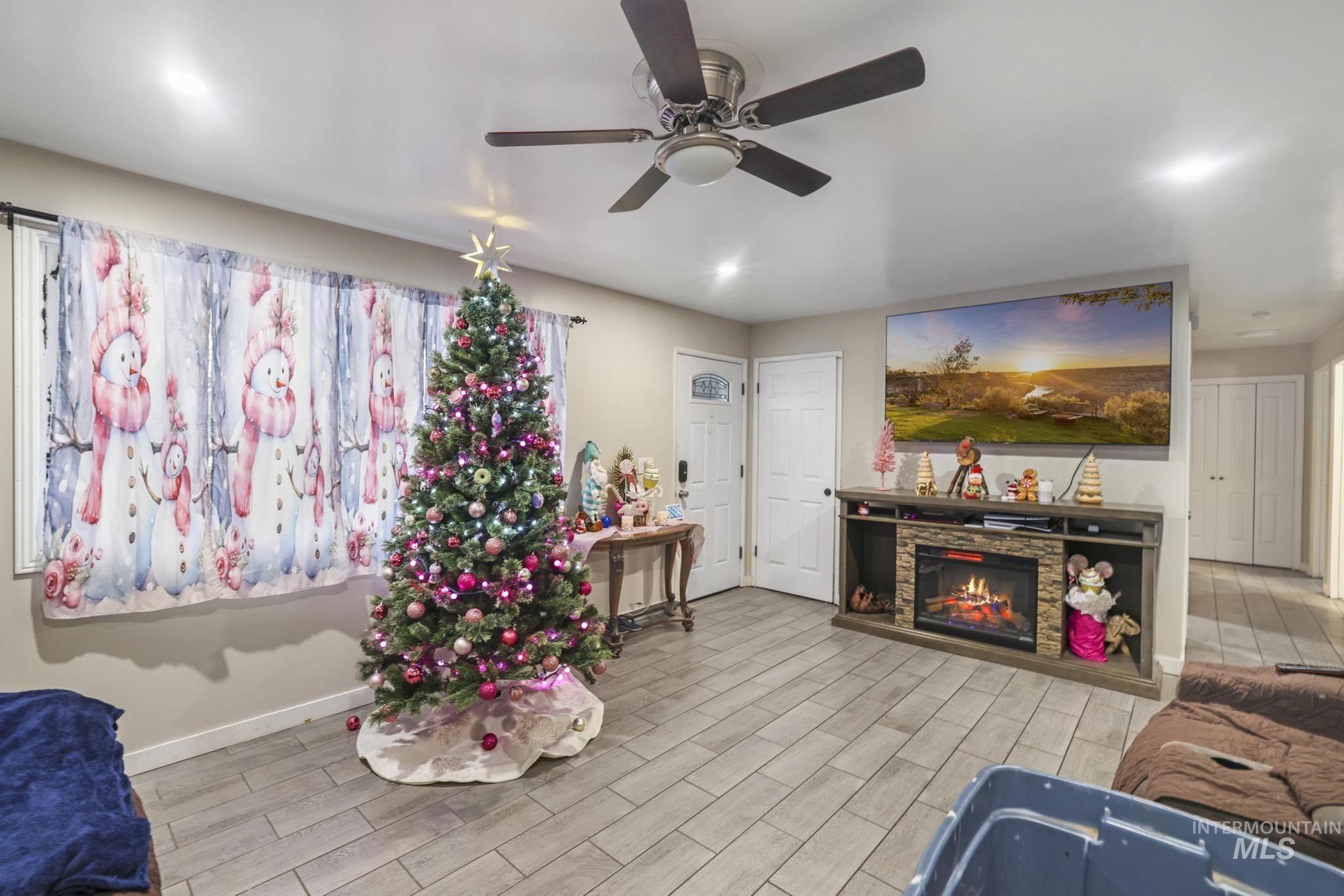 Living room with wood finish floors, a stone fireplace, and ceiling fan