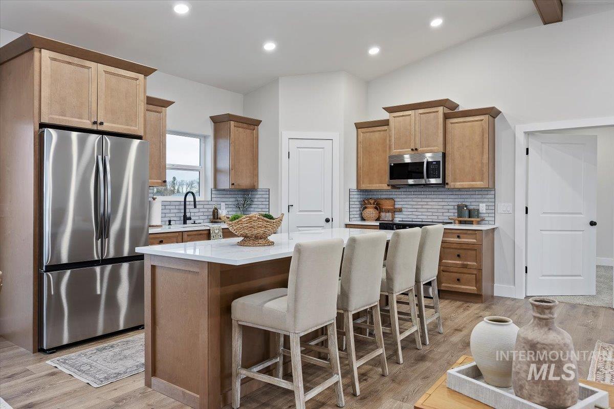 Kitchen featuring stainless steel appliances, a kitchen island, a kitchen bar, tasteful backsplash, and lofted ceiling