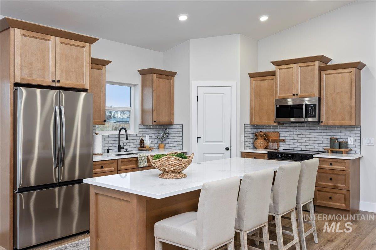 Kitchen featuring stainless steel appliances, backsplash, a kitchen bar, and light wood finished floors