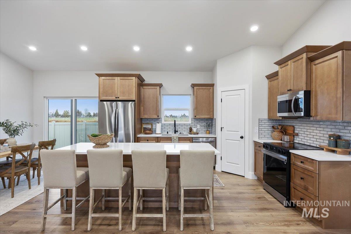 Kitchen featuring appliances with stainless steel finishes, decorative backsplash, a kitchen island, light wood-type flooring, and a kitchen bar