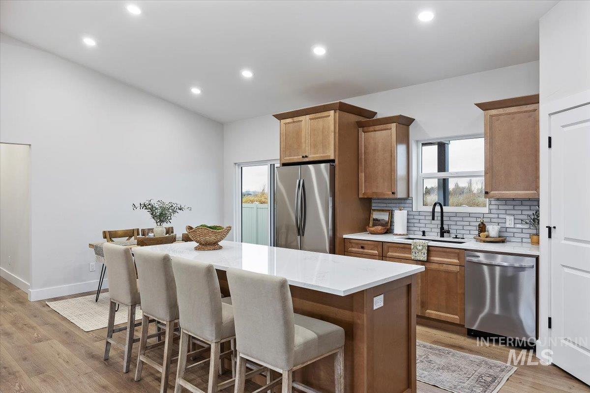 Kitchen with tasteful backsplash, appliances with stainless steel finishes, light wood-style flooring, a breakfast bar area, and brown cabinets