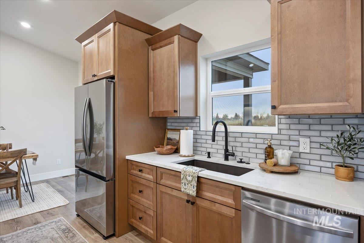 Kitchen featuring appliances with stainless steel finishes, light stone counters, light wood-style floors, tasteful backsplash, and recessed lighting
