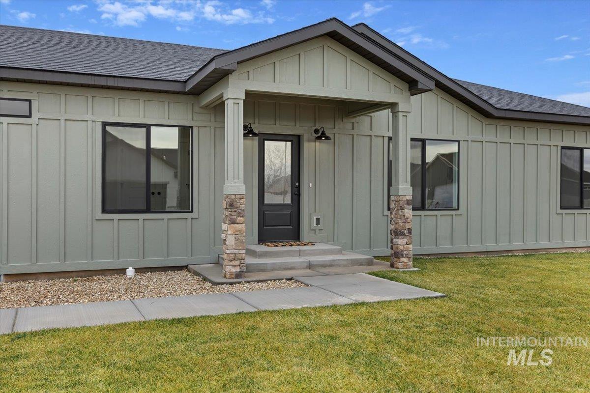 Doorway to property with board and batten siding, roof with shingles, and a yard