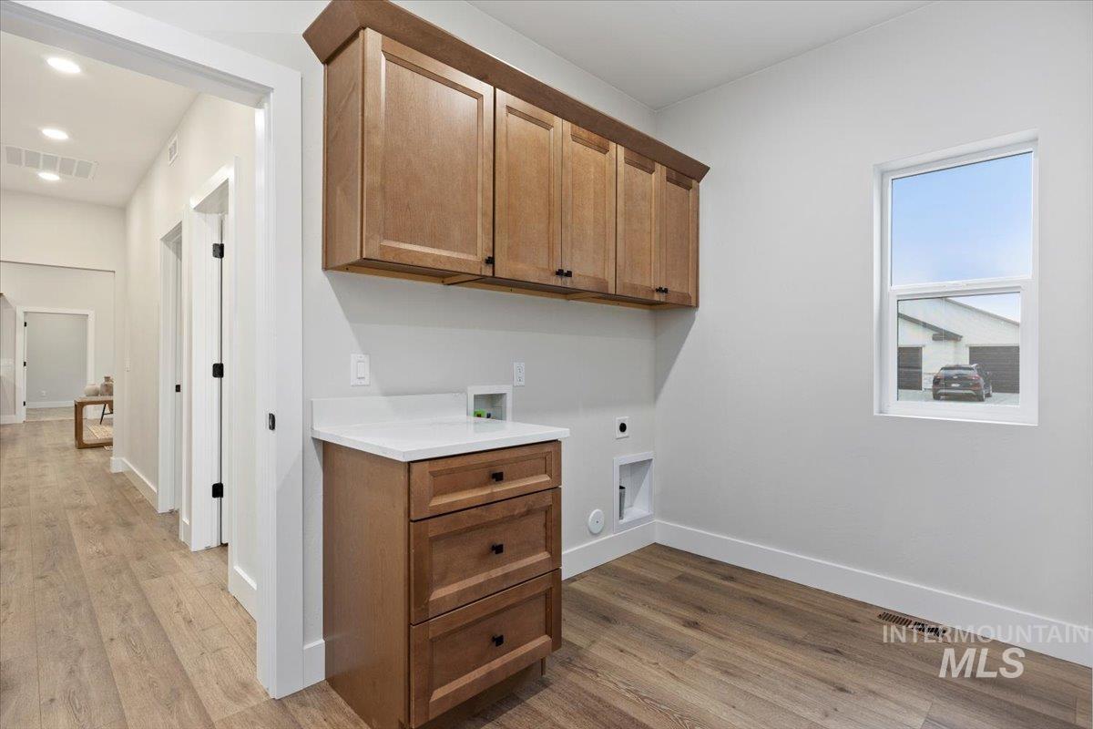 Laundry area featuring electric dryer hookup, cabinet space, hookup for a washing machine, and light wood finished floors