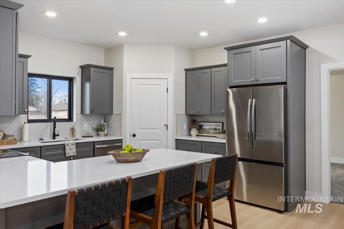 Kitchen with gray cabinetry, stainless steel appliances, a breakfast bar area, backsplash, and a peninsula