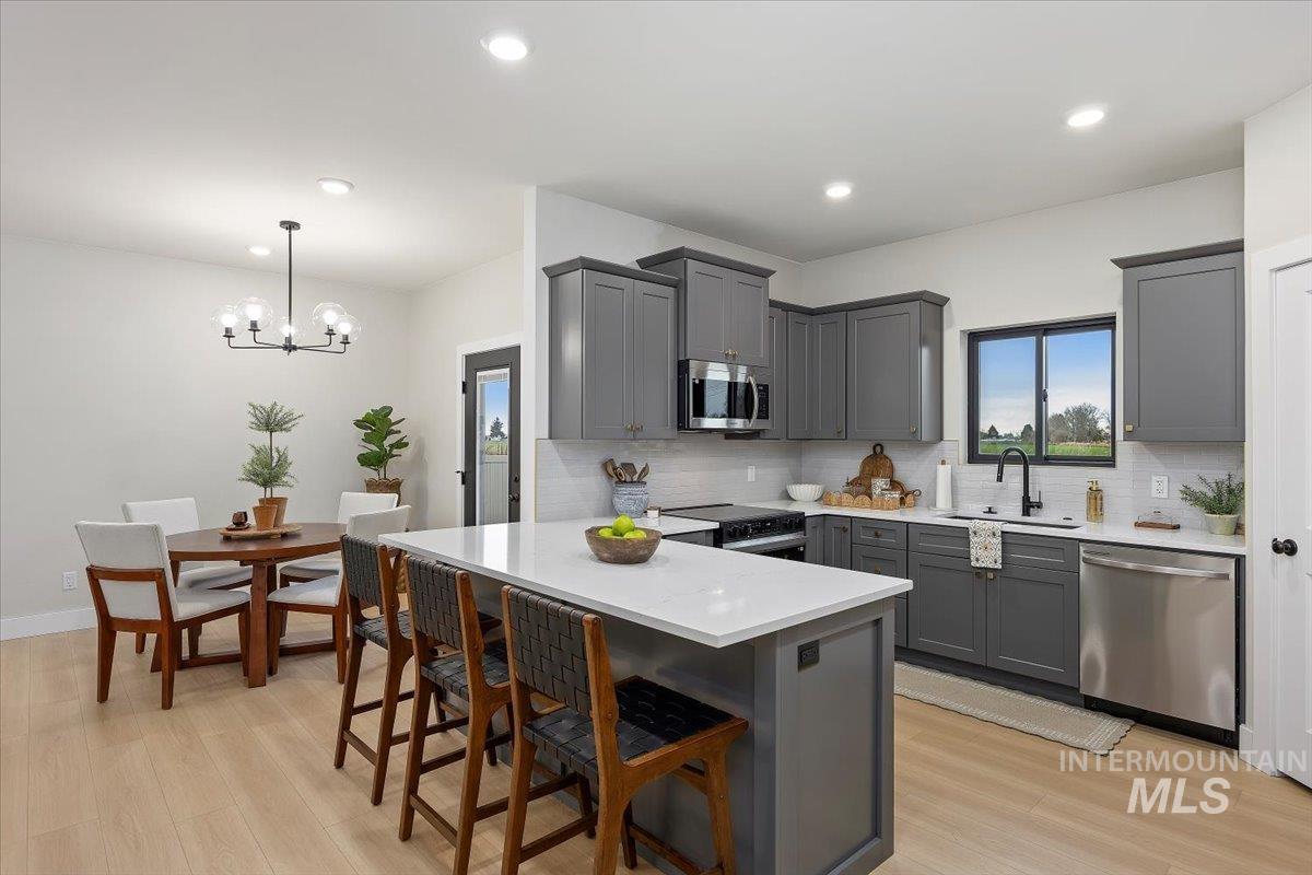 Kitchen with gray cabinetry, a peninsula, a kitchen bar, pendant lighting, and appliances with stainless steel finishes
