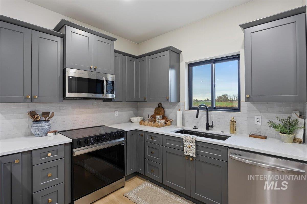 Kitchen featuring gray cabinets, appliances with stainless steel finishes, light stone counters, and decorative backsplash
