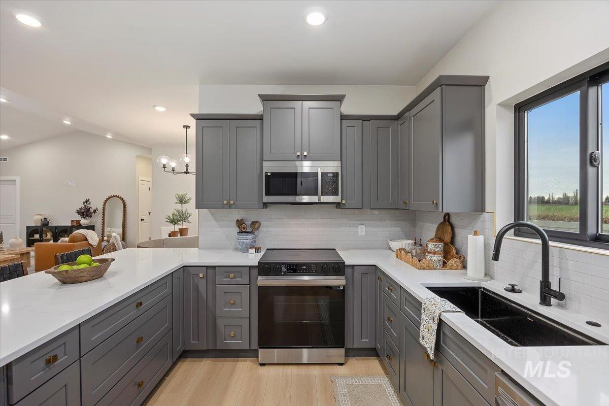 Kitchen with gray cabinetry, black electric range oven, stainless steel microwave, light stone countertops, and recessed lighting