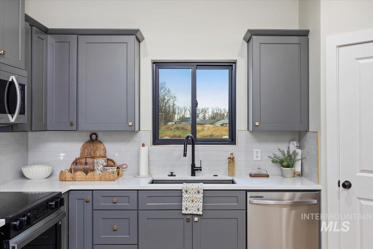 Kitchen featuring gray cabinetry, appliances with stainless steel finishes, light stone counters, and tasteful backsplash