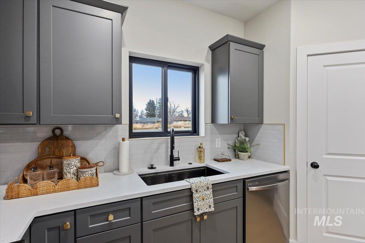 Kitchen featuring gray cabinetry, dishwasher, light stone counters, and backsplash