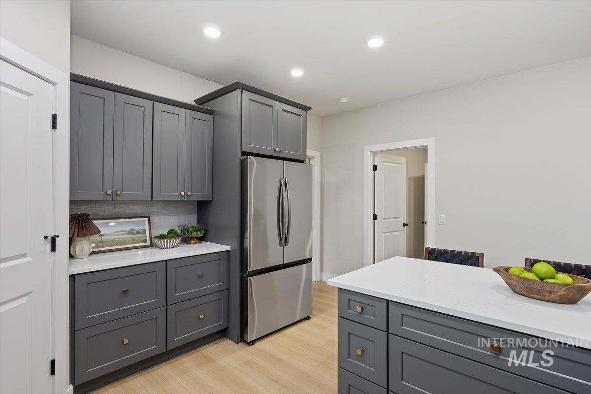 Kitchen featuring gray cabinetry, freestanding refrigerator, light wood-type flooring, tasteful backsplash, and light stone countertops