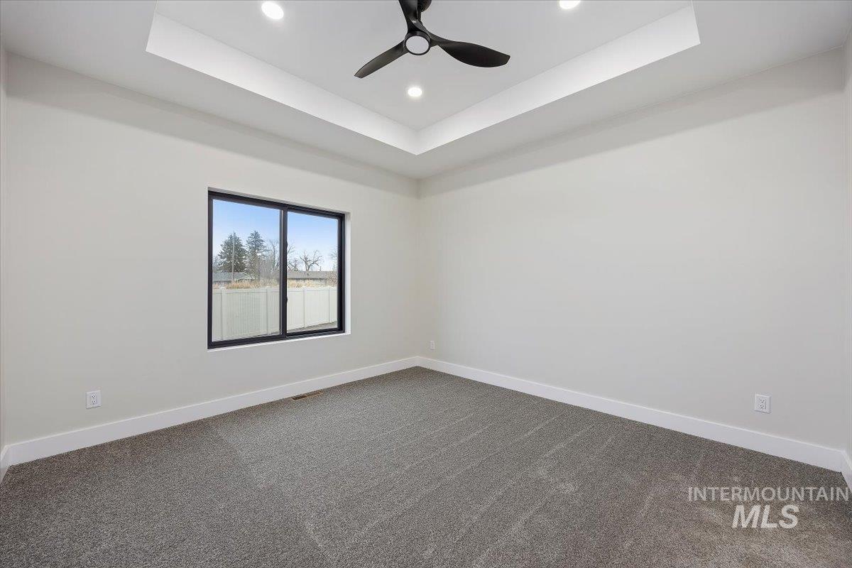 Empty room with a tray ceiling, dark carpet, a ceiling fan, and recessed lighting