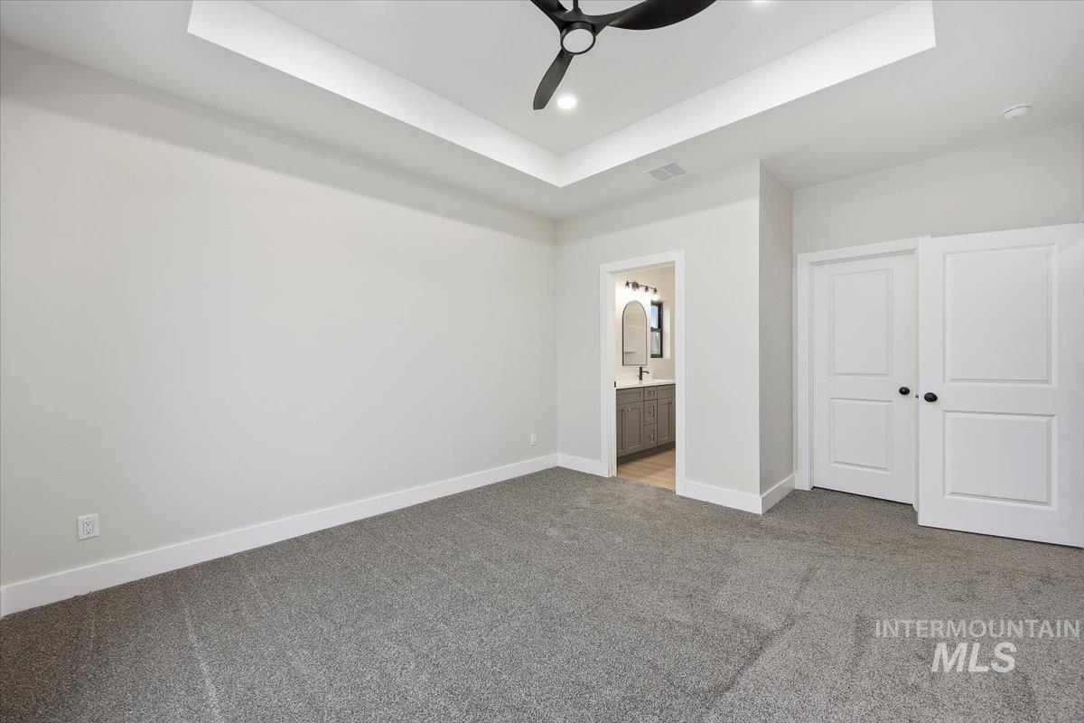 Unfurnished bedroom featuring a raised ceiling, ensuite bathroom, carpet, recessed lighting, and a ceiling fan