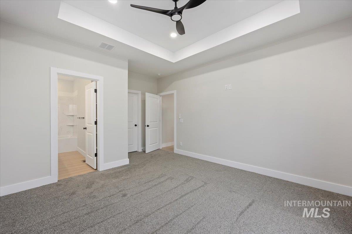 Unfurnished bedroom with a raised ceiling, light colored carpet, a ceiling fan, recessed lighting, and connected bathroom