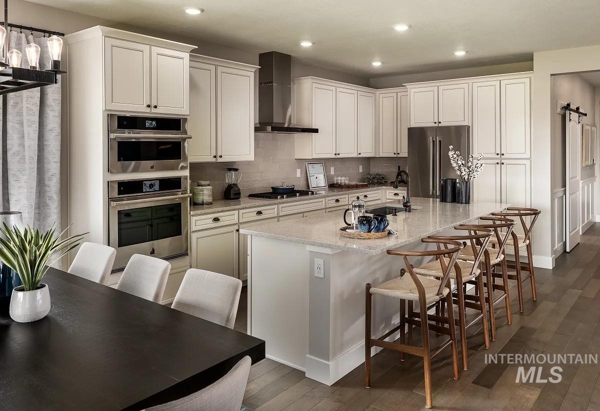 Kitchen featuring a kitchen bar, light stone countertops, wall chimney exhaust hood, an island with sink, and appliances with stainless steel finishes