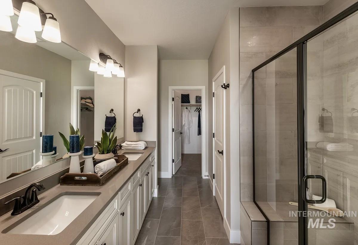 Full bathroom with double vanity, a shower stall, a spacious closet, and dark tile patterned flooring