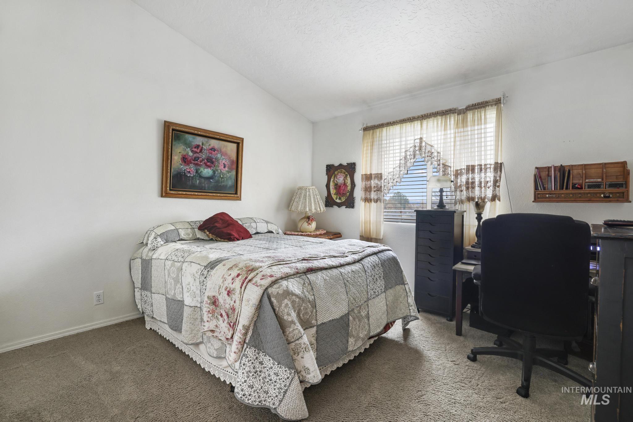 Bedroom featuring vaulted ceiling, an office area, carpet, and a textured ceiling
