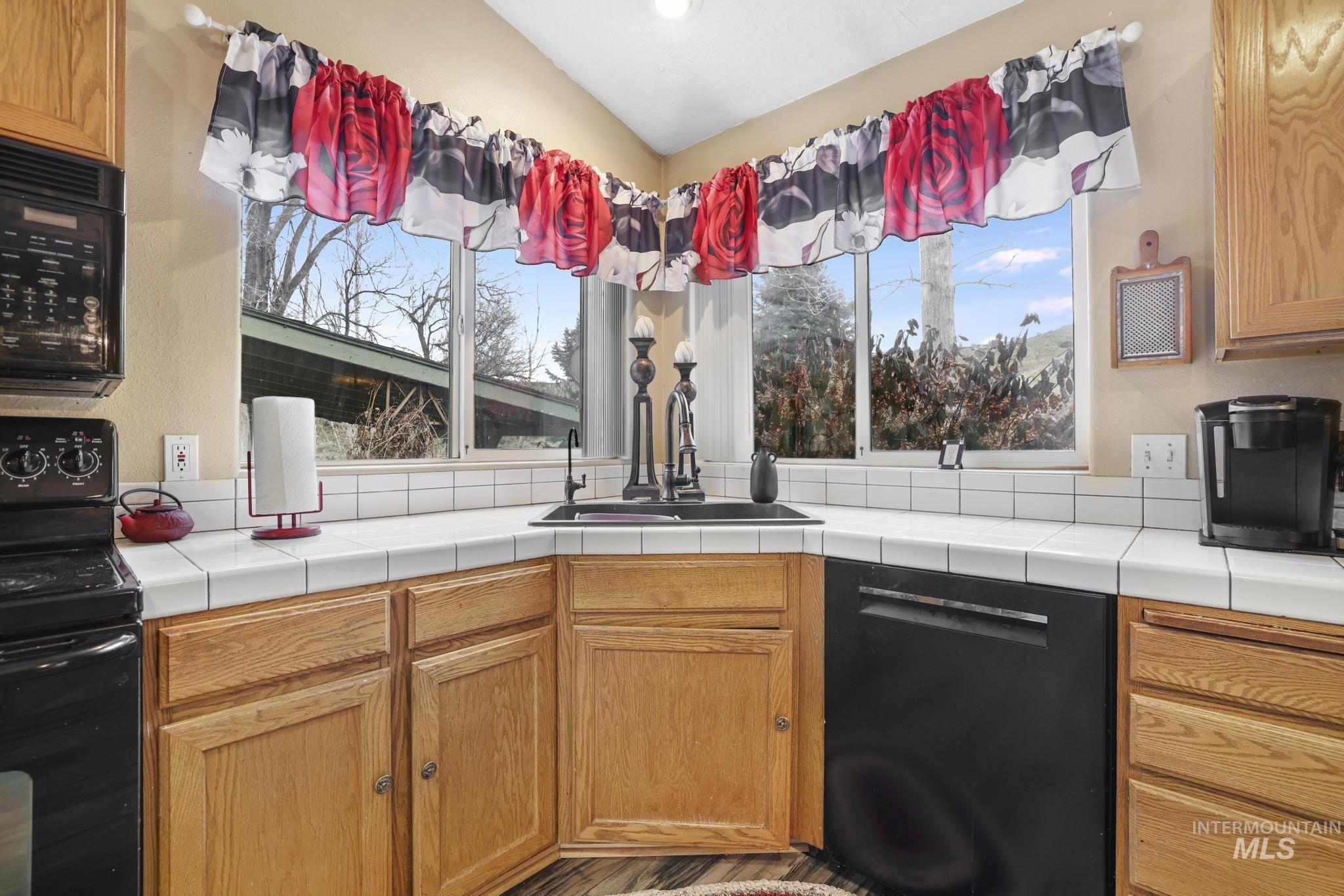 Kitchen with black appliances, tile counters, plenty of natural light, and brown cabinetry