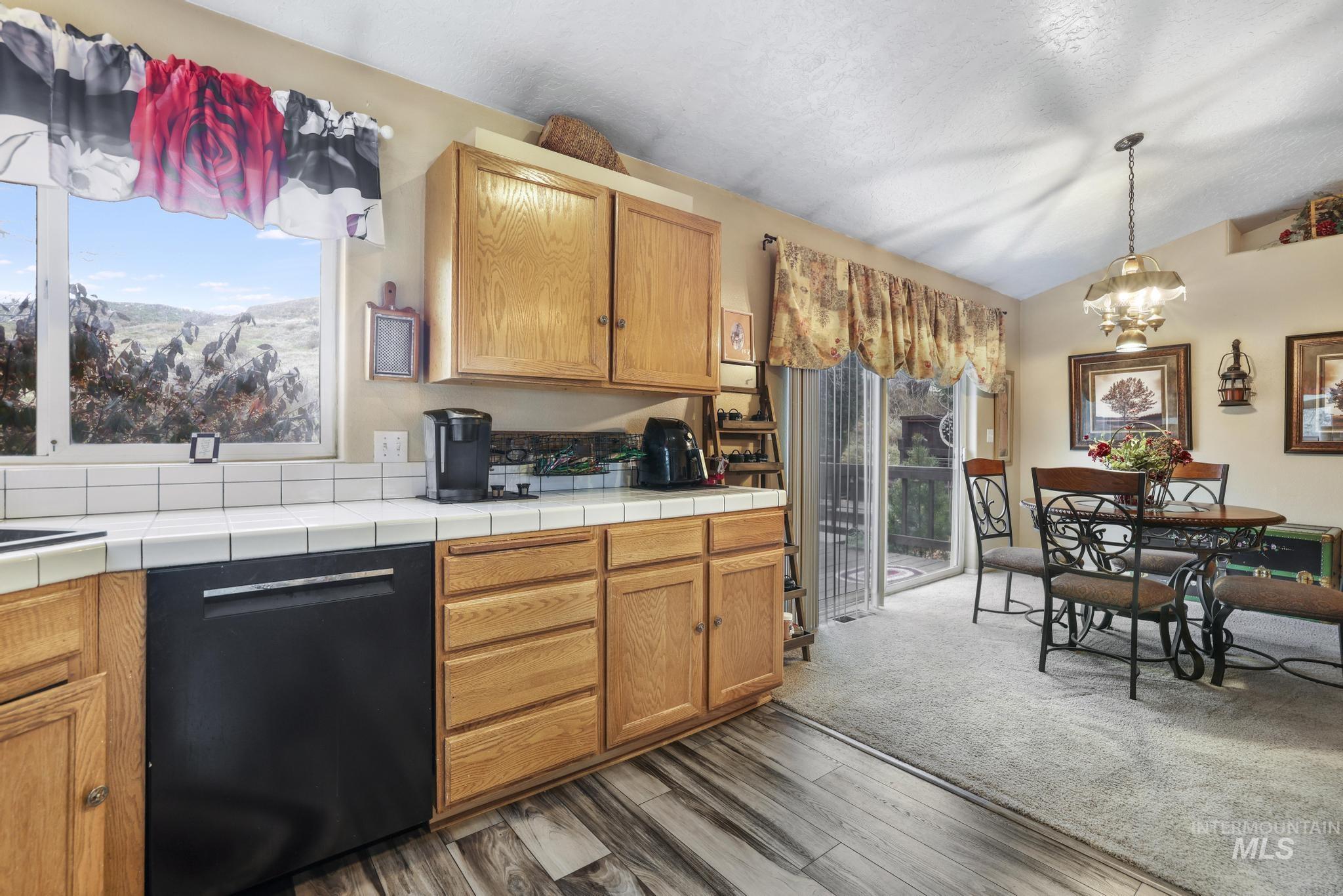 Kitchen featuring black dishwasher, a chandelier, vaulted ceiling, tile counters, and brown cabinetry