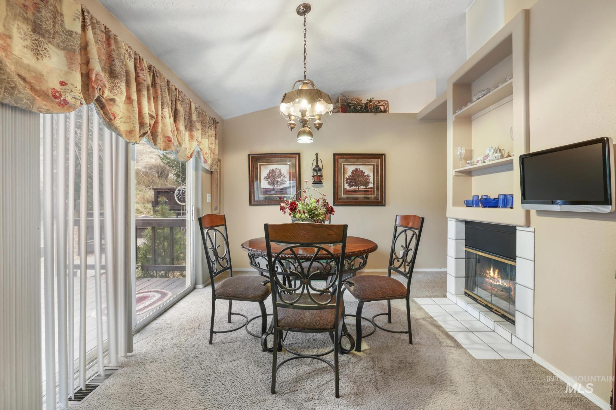 Dining room featuring lofted ceiling, light colored carpet, a chandelier, and a fireplace with flush hearth