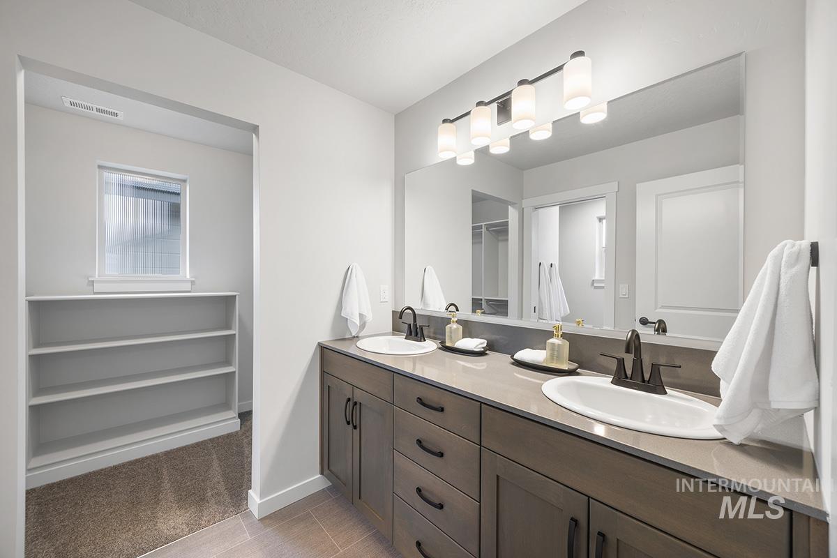Bathroom featuring double vanity, a spacious closet, and light carpet