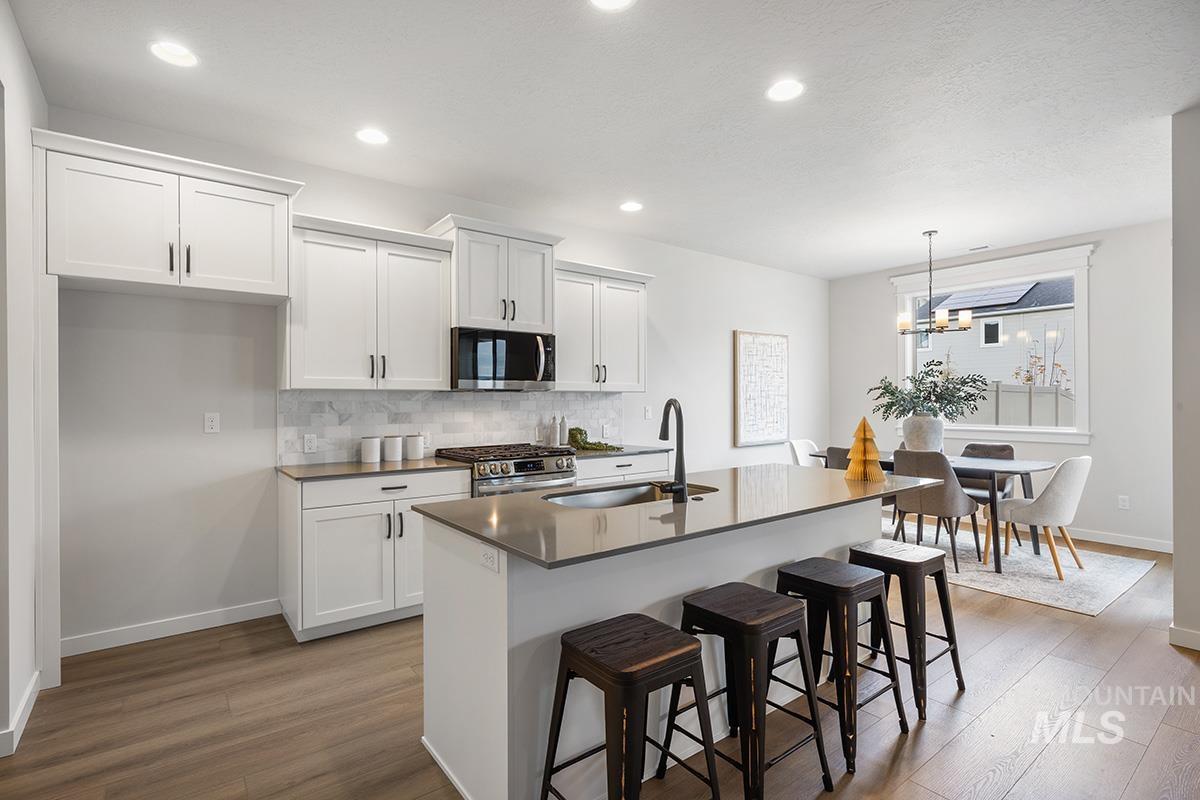 Kitchen with white cabinets, stainless steel appliances, a kitchen bar, dark wood finished floors, and recessed lighting