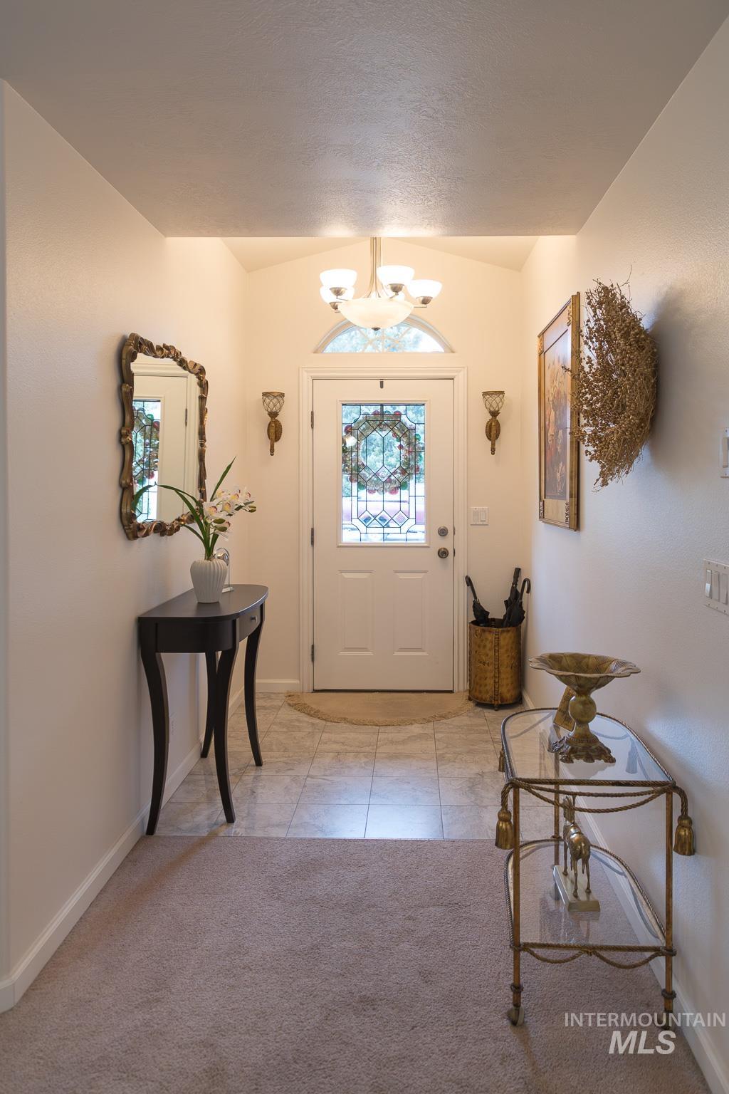 Foyer entrance featuring light carpet, a chandelier, vaulted ceiling, and light tile patterned floors