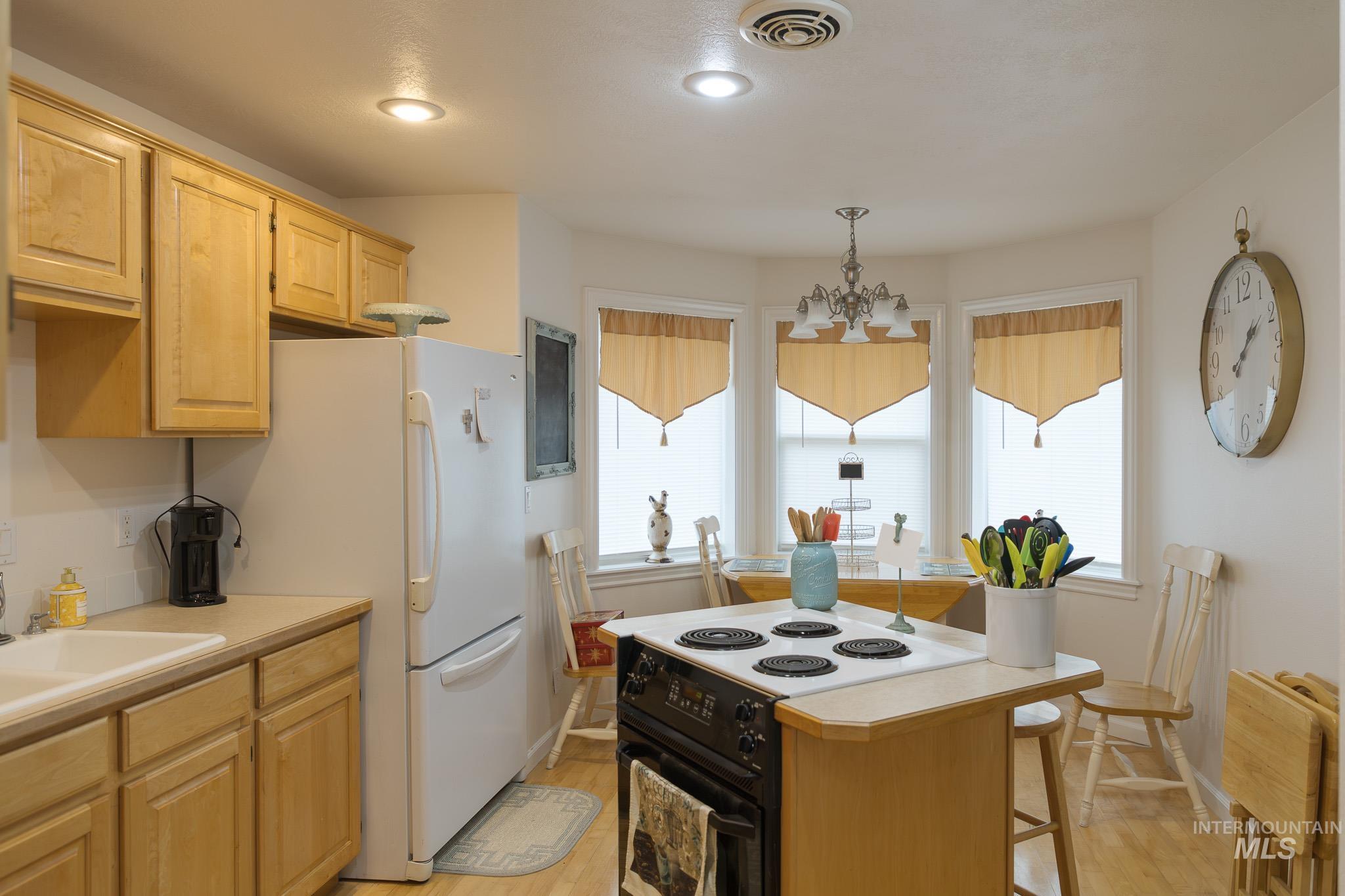 Kitchen with black electric range, light countertops, a kitchen island, light wood finished floors, and light brown cabinetry