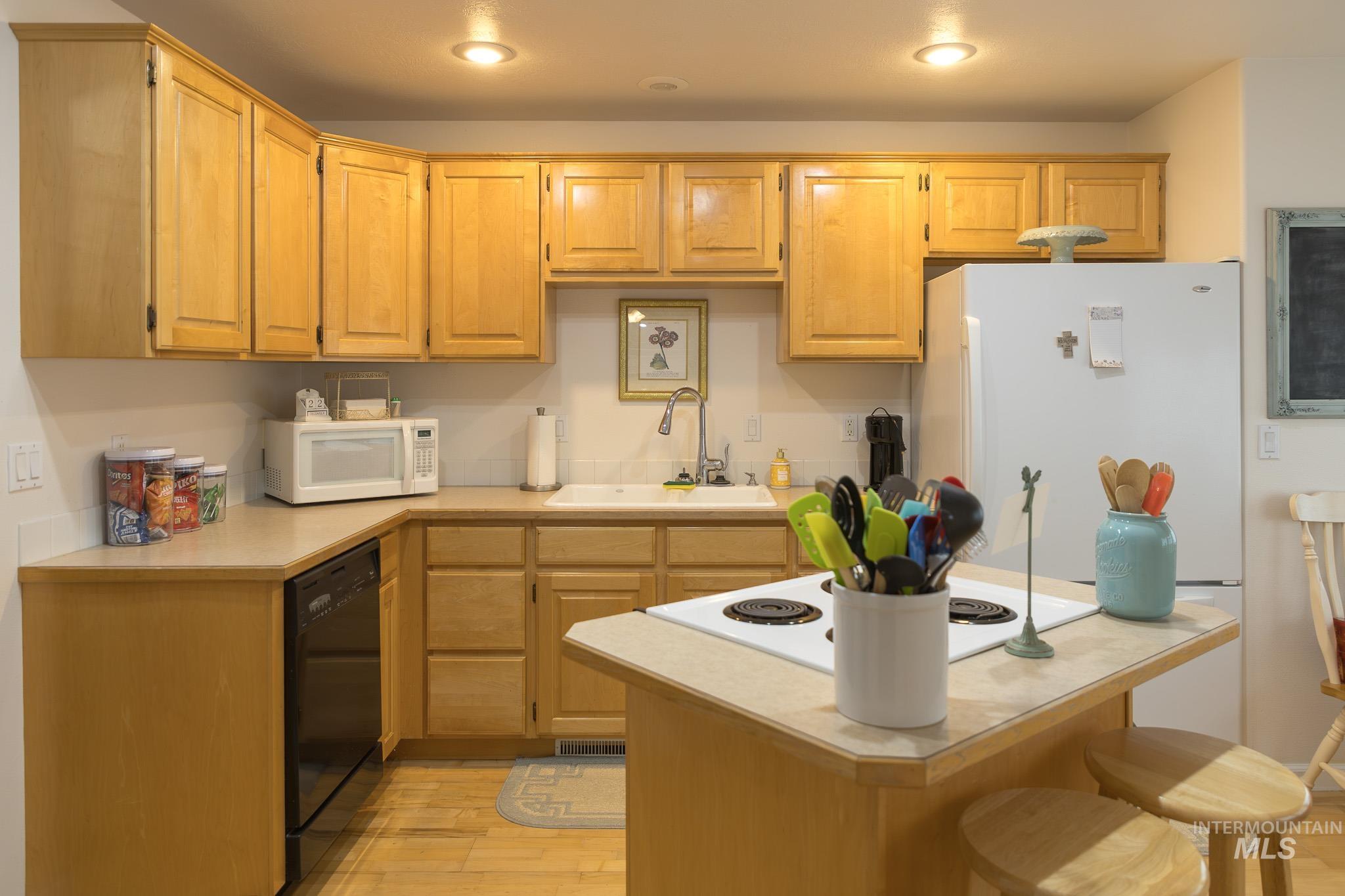 Kitchen featuring light countertops, a breakfast bar area, light wood-style flooring, white appliances, and recessed lighting