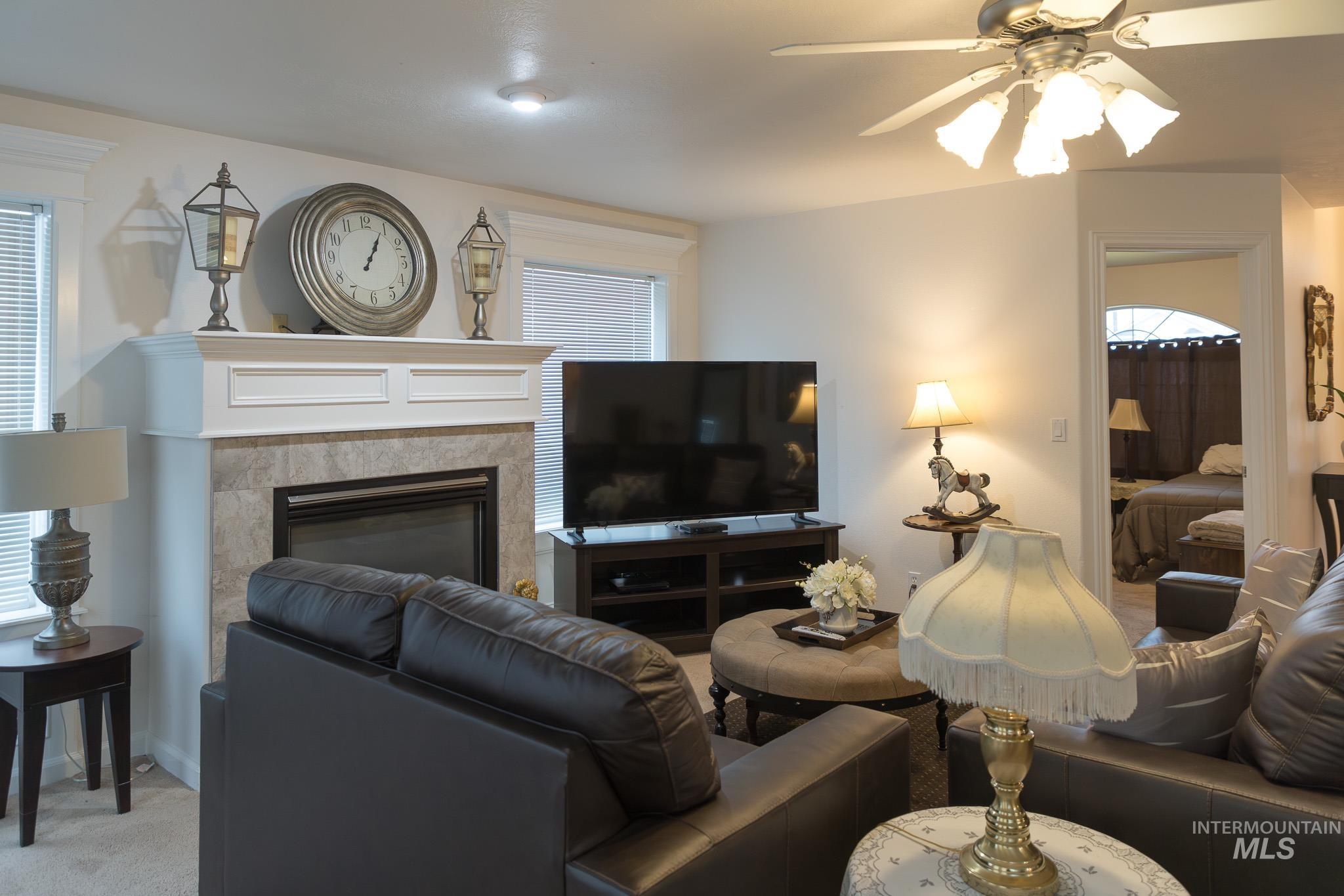 Living room with a tiled fireplace, a ceiling fan, plenty of natural light, and carpet flooring