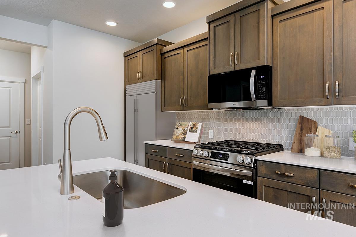 Kitchen featuring stainless steel appliances, backsplash, recessed lighting, light stone counters, and dark brown cabinetry