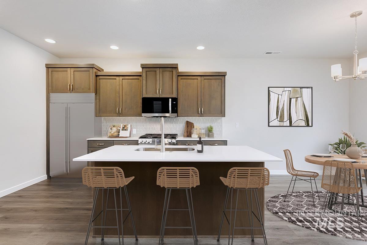Kitchen featuring an island with sink, stainless steel appliances, a breakfast bar area, decorative light fixtures, and decorative backsplash