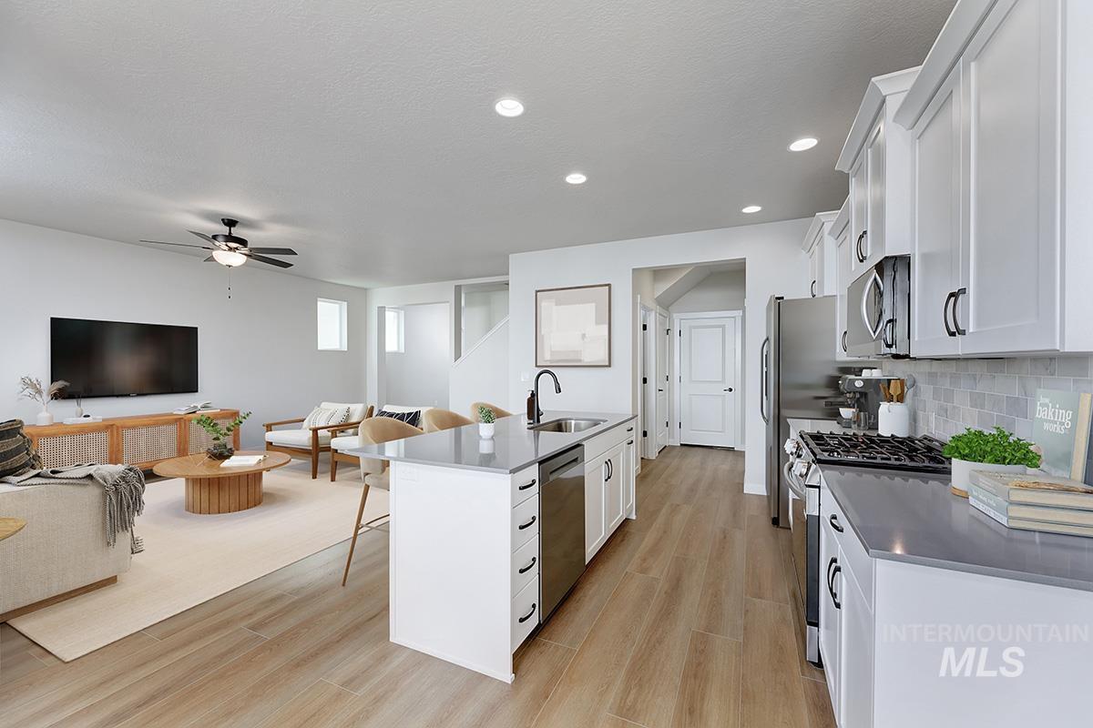 Kitchen with stainless steel appliances, open floor plan, white cabinets, wood finish floors, and a breakfast bar
