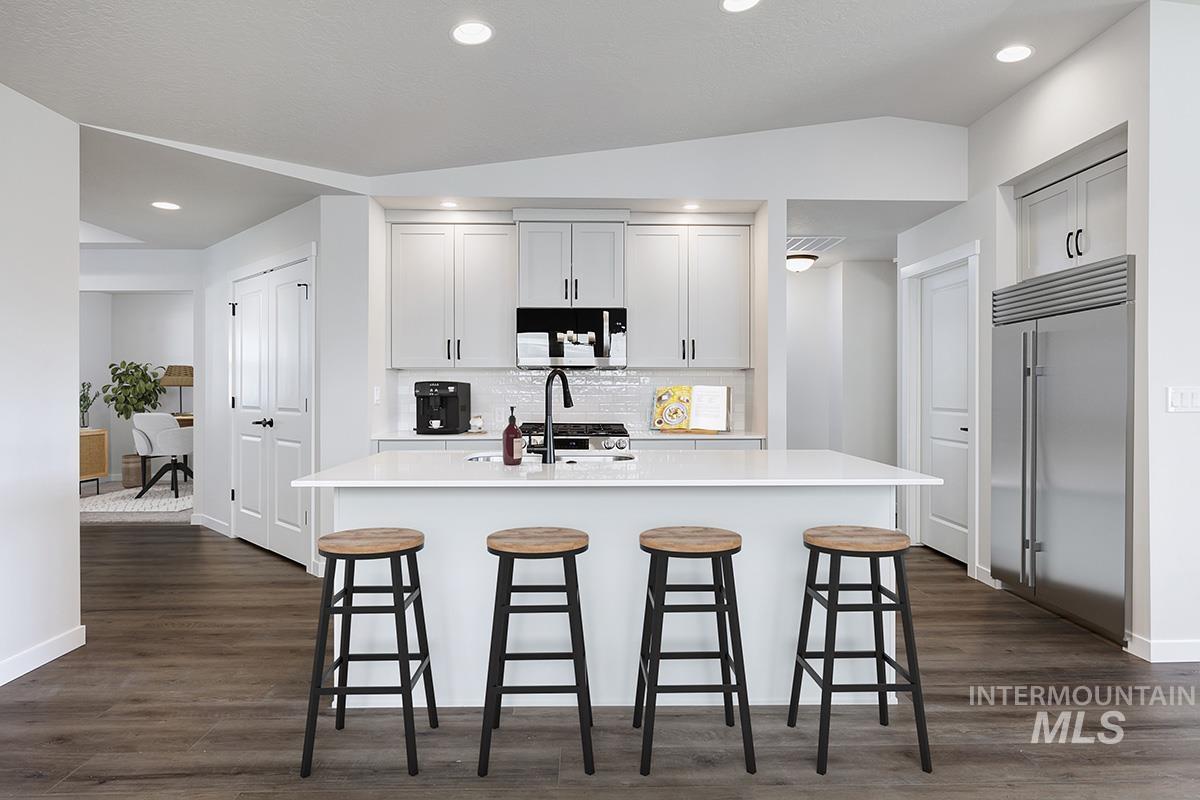 Kitchen featuring built in refrigerator, a center island with sink, a breakfast bar area, lofted ceiling, and tasteful backsplash