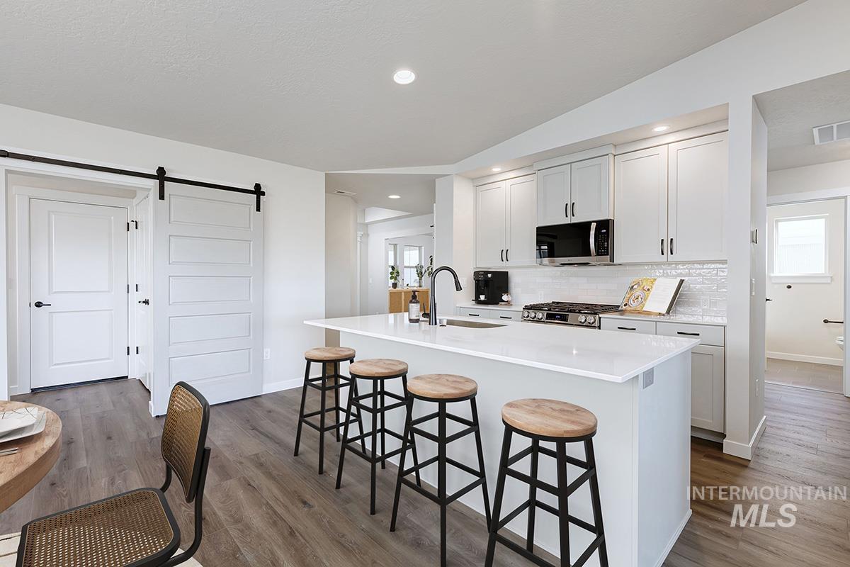 Kitchen featuring a barn door, a breakfast bar area, lofted ceiling, dark wood finished floors, and an island with sink