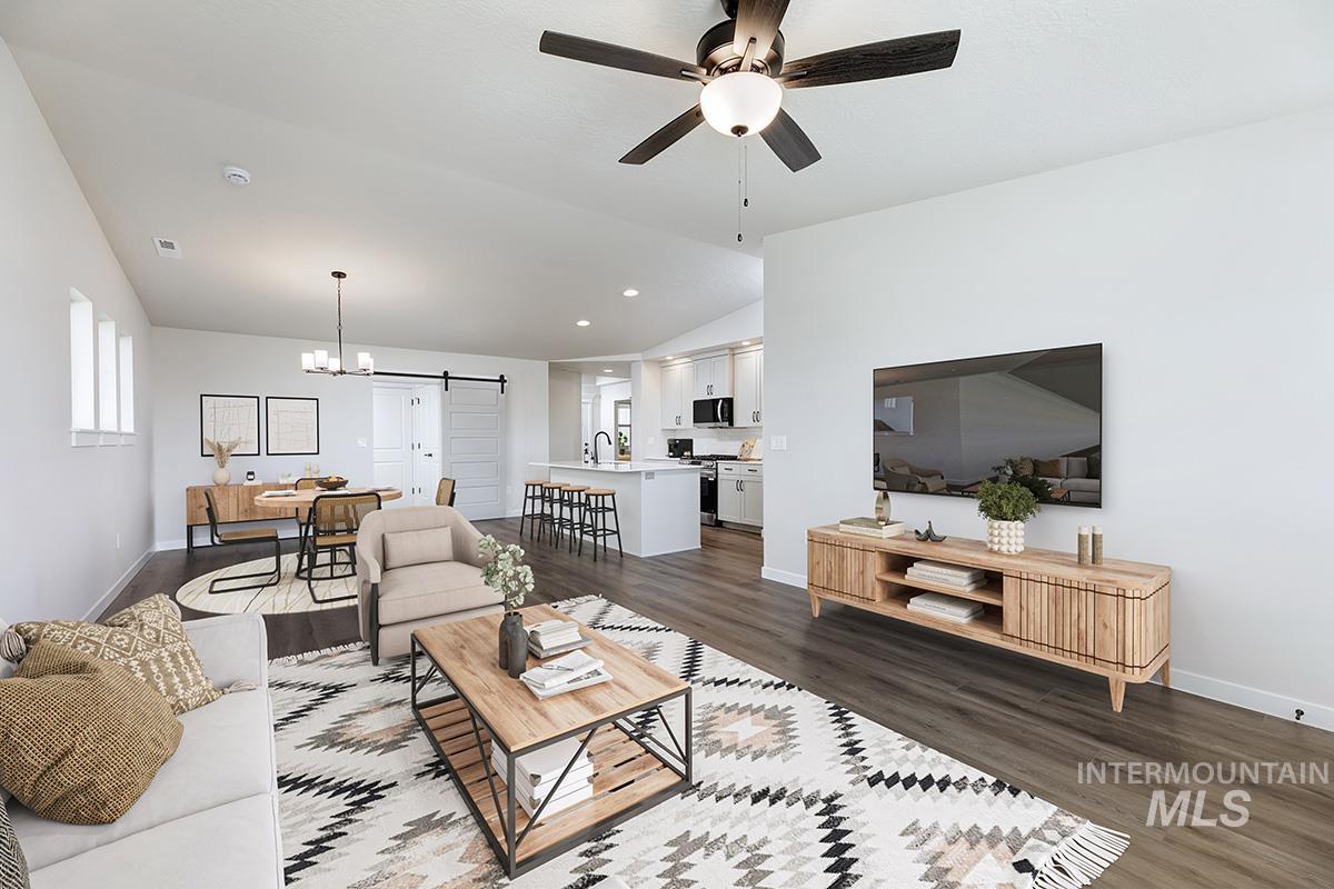 Living room with a barn door, vaulted ceiling, a chandelier, dark wood-style floors, and ceiling fan