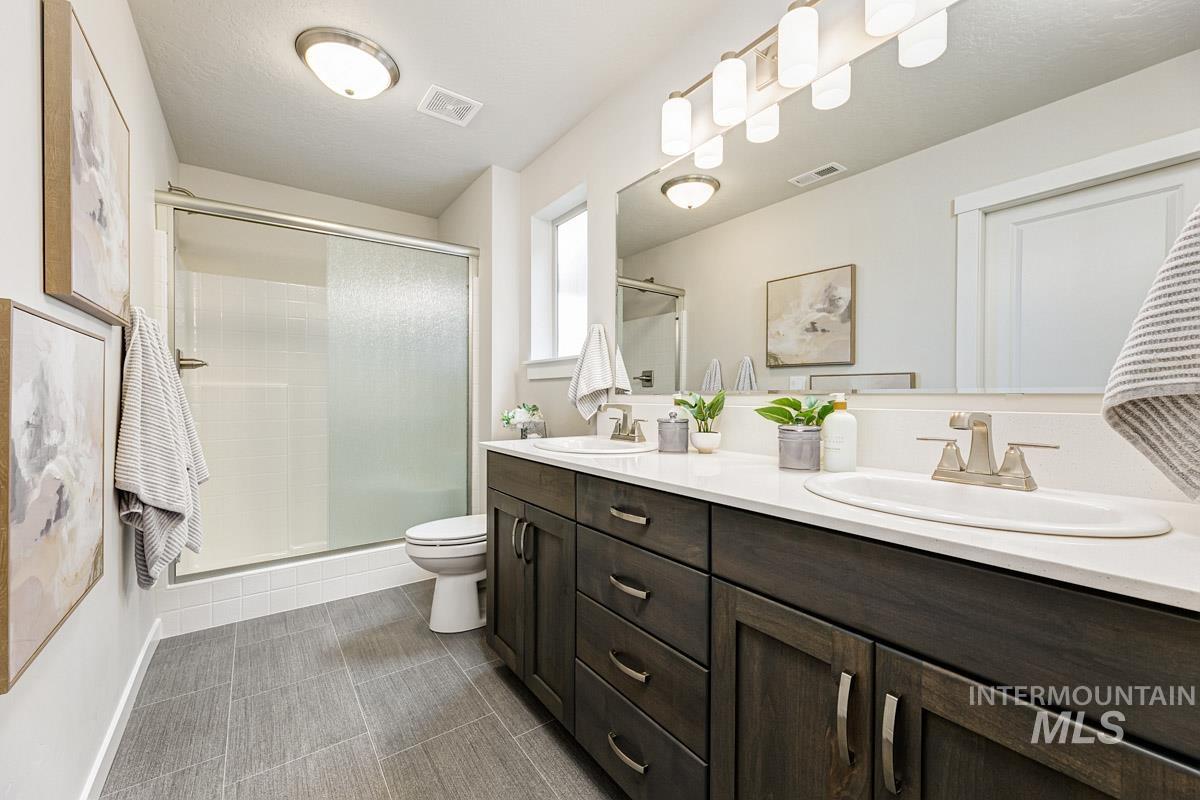 Full bath with double vanity, a stall shower, and dark tile patterned flooring
