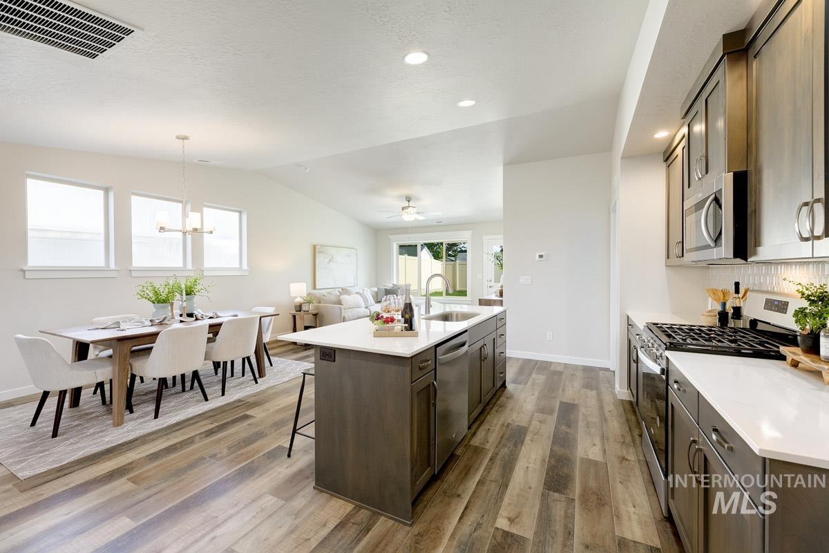 Kitchen featuring appliances with stainless steel finishes, dark brown cabinets, hanging light fixtures, an island with sink, and a kitchen breakfast bar