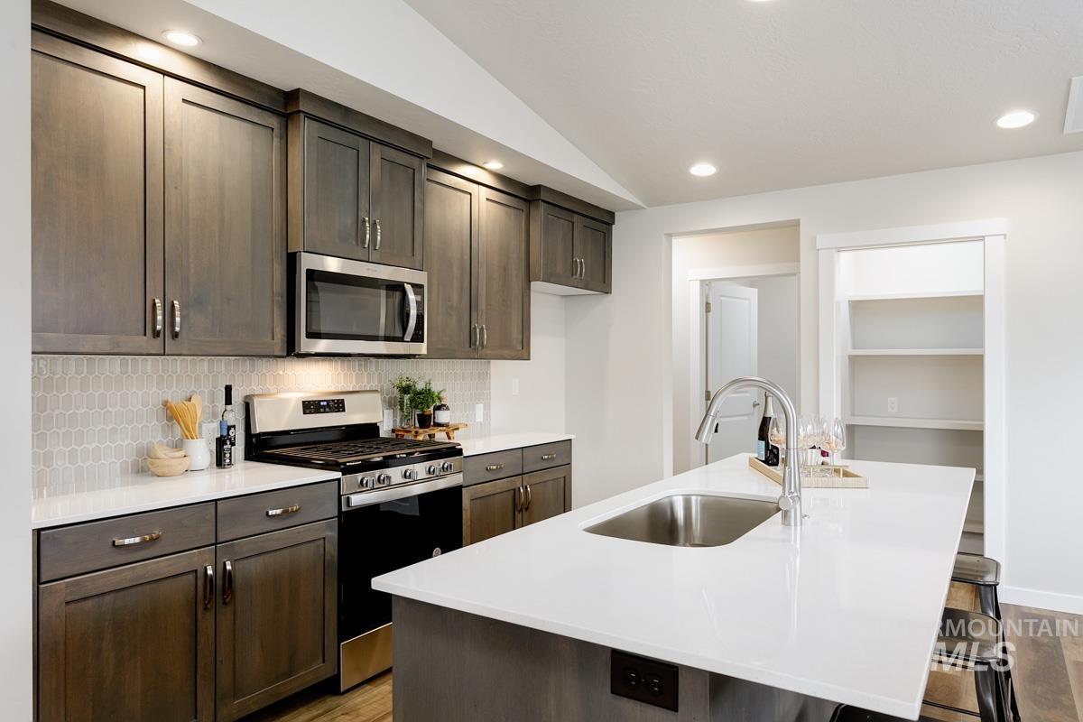 Kitchen with appliances with stainless steel finishes, a kitchen bar, a kitchen island with sink, dark brown cabinetry, and backsplash