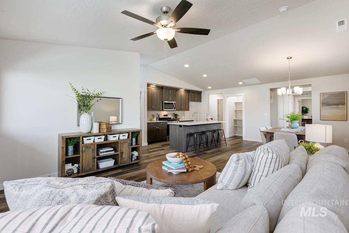 Living room featuring dark wood-style flooring, vaulted ceiling, ceiling fan, a chandelier, and recessed lighting